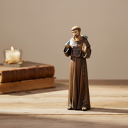 Statue of a religious figure on a wooden surface with a candle and books in the background