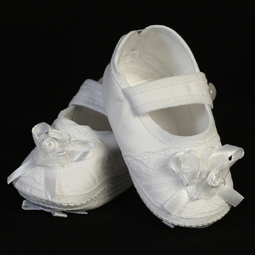 White baptism shoes with decorative bows on a black background