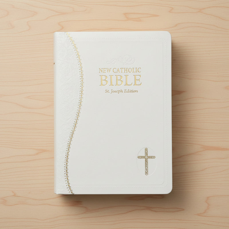 White Bible with gold text and cross on a wooden surface