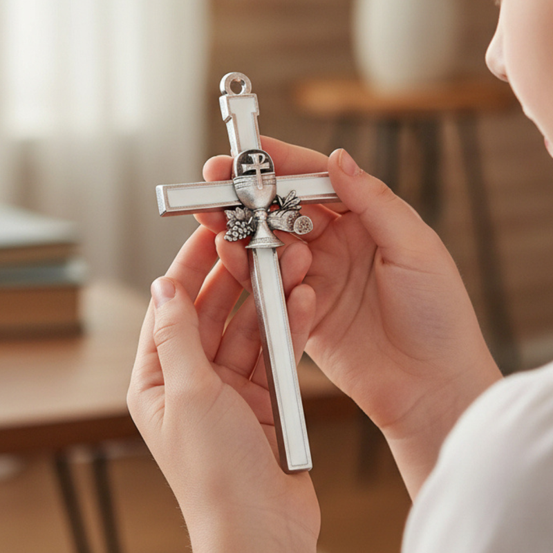 A child's hands hold a white enameled First Communion gift cross with a chalice emblem.