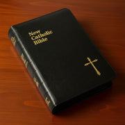 Black New Catholic Bible with gold text and cross on a wooden surface