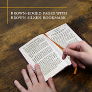 Open book with brown-edged pages and a brown silken bookmark on a wooden surface.