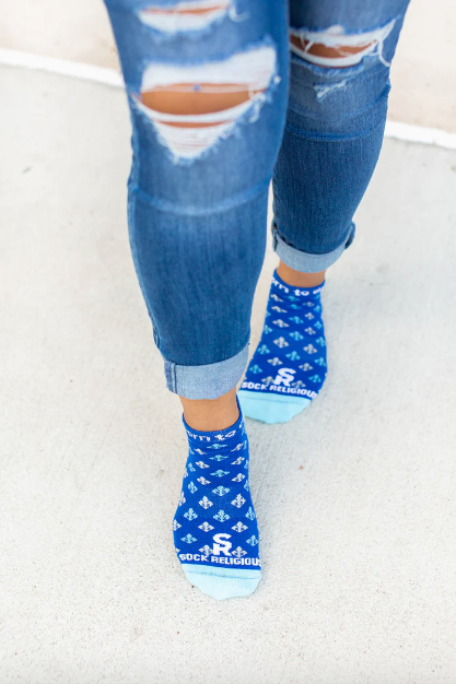 Person wearing blue St. Joan of Arc socks with a fleur-de-lis print