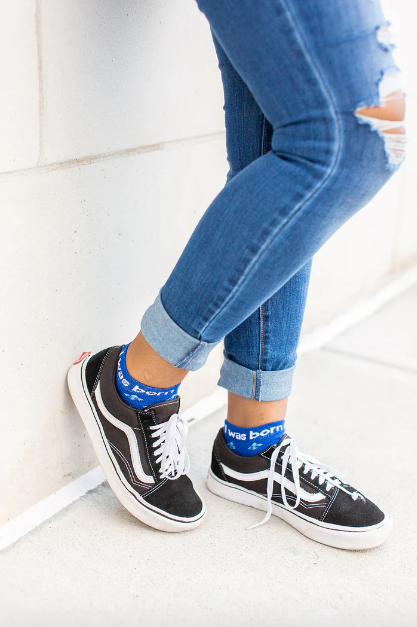 Person wearing blue St. Joan of Arc socks with a fleur-de-lis print
