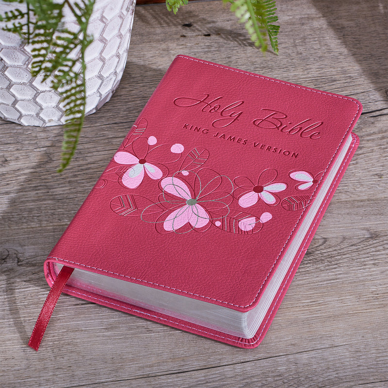 A pink faux leather compact Bible with a floral design and the text 'Holy Bible King James Version' on the cover. The Bible is presented in a flexible cover format with a satin ribbon marker.