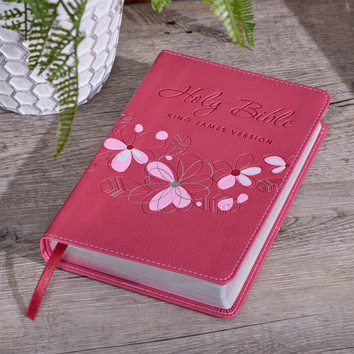 A pink faux leather compact Bible with a floral design and the text 'Holy Bible King James Version' on the cover. The Bible is presented in a flexible cover format with a satin ribbon marker.