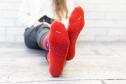 Person wearing blue and red patterned socks with St. Augustine and flaming hearts, on a wooden floor.