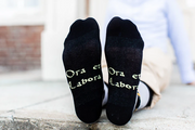 Gray socks with St. Benedict design worn by a person on a light gray pavement background