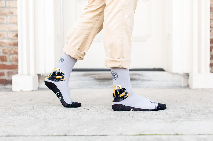 Gray socks with St. Benedict design worn by a person on a light gray pavement background