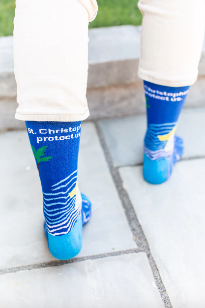 Person wearing blue socks with images of St. Christopher carrying the Infant Jesus through water