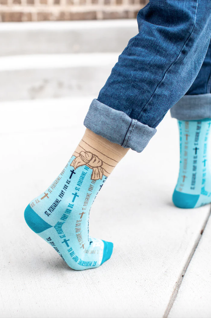 Light blue St. Peregrine-themed socks with text and cross designs worn with rolled-up jeans