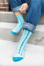 Light blue St. Peregrine-themed socks with text and cross designs worn with rolled-up jeans
