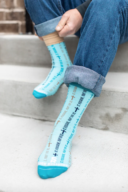 Light blue St. Peregrine-themed socks with text and cross designs worn with rolled-up jeans