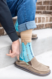 Light blue St. Peregrine-themed socks with text and cross designs worn with rolled-up jeans