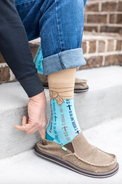 Light blue St. Peregrine-themed socks with text and cross designs worn with rolled-up jeans