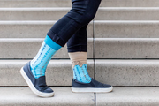 Light blue St. Peregrine-themed socks with text and cross designs worn with rolled-up jeans
