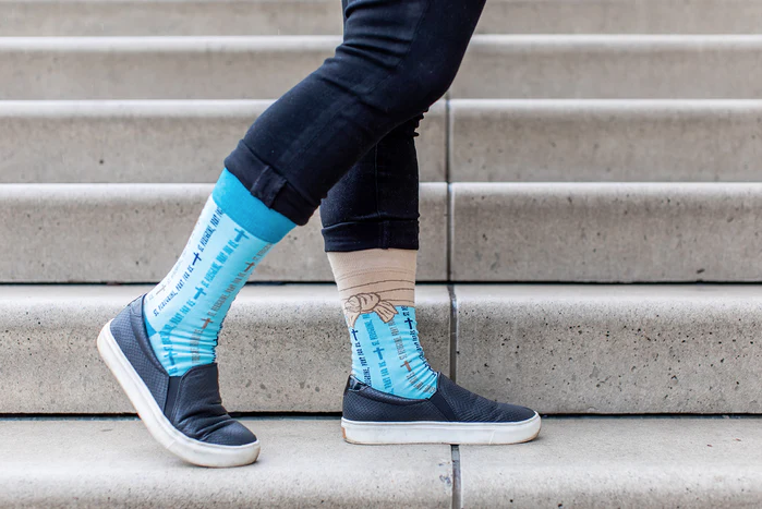Light blue St. Peregrine-themed socks with text and cross designs worn with rolled-up jeans
