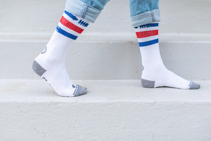 White St. Sebastian socks with blue and red stripes worn with light blue jeans on a light gray background