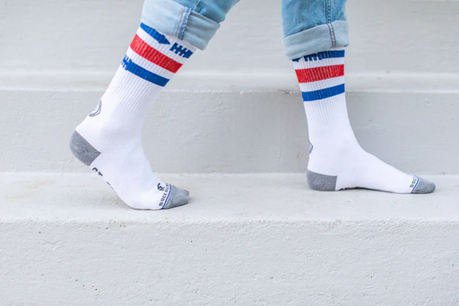 White St. Sebastian socks with blue and red stripes worn with light blue jeans on a light gray background