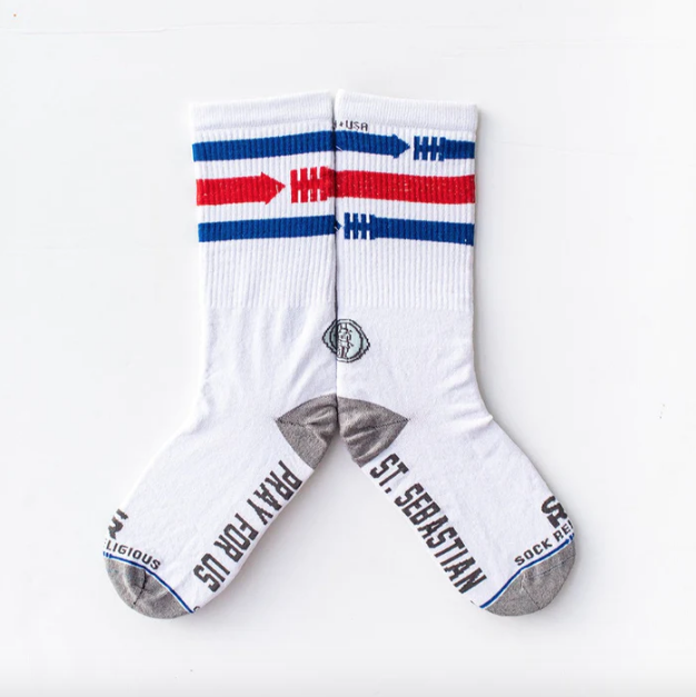 A pair of white socks with red and blue athletic design featuring arrows and a St. Sebastian medal above the heel.