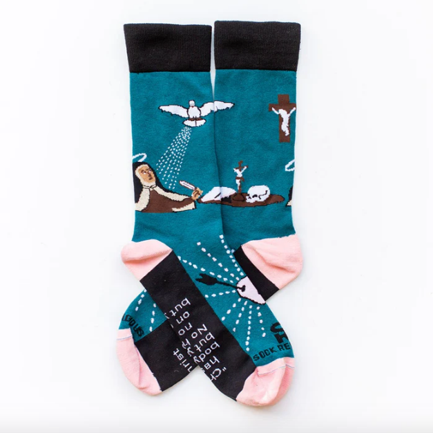A pair of socks with a design featuring St. Teresa of Avila, with colors including blue, black, pink, and white, and various symbols and text related to the saint.
