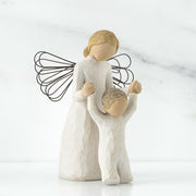 A figurine of a guardian angel, with a resin and metal construction, depicted in a praying posture alongside a child.